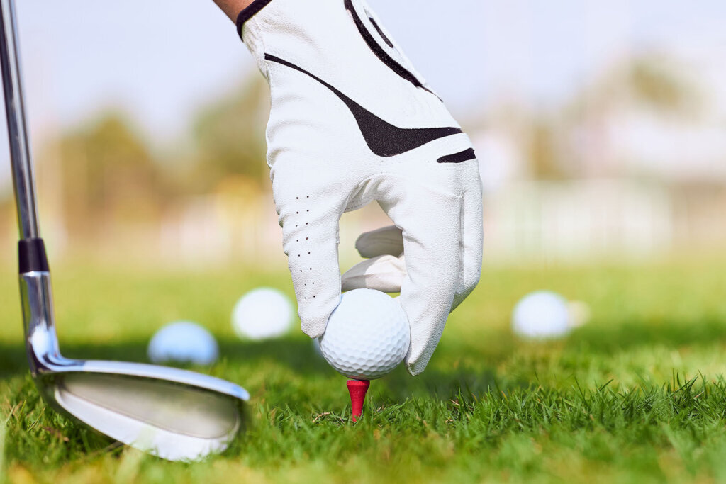 Golfer's hand putting a golf ball on tee in golf course.