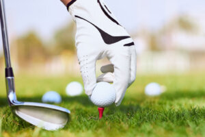 Golfer's hand putting a golf ball on tee in golf course.