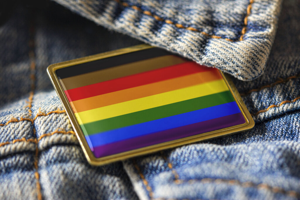 Philadelphia people of color inclusive flag pin on a denim jacket for LGBTQ identity, pride, and activism. The intersectional flag design is public domain for all uses.