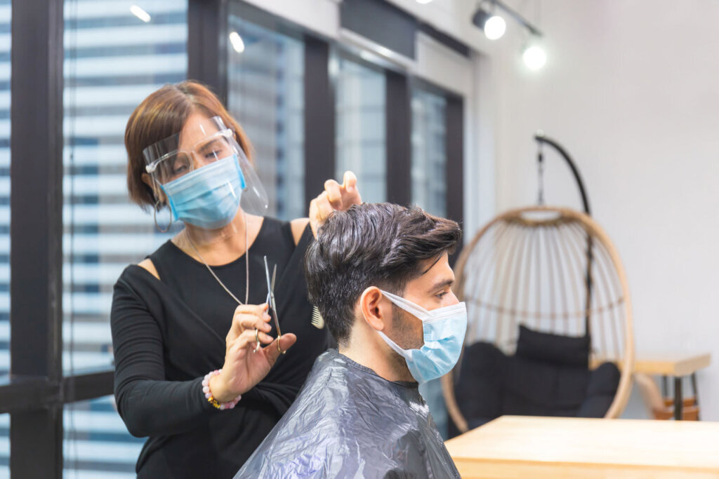 Young man getting haircut by hairdresser, Barber using scissors and comb, New normal concept