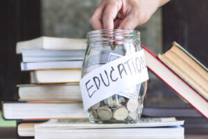 Coins and banknote in a glass jar placed on the textbook.