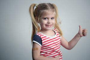 Child vaccination. Little girl showing thumb up gesure and adhezive arm bandage, studio shot.