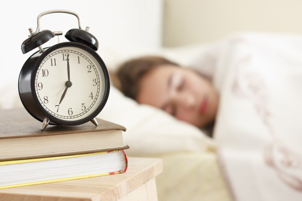 Teenager girl sleeping in a white bed. Alarm clock in the foreground on a pile of books