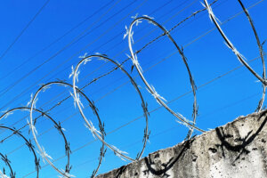 Barbed wire and electric fence, like a prison wall, with a blue sky