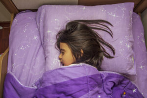 Top view of sleeping girl hugging her duvet on her bed