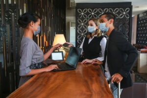 Couple and receptionist at counter in hotel wearing medical masks as precaution against virus. Couple on a business trip doing check in at the hotel