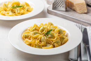 Plates with tortelloni stuffed with spinach and ricotta, stir fried with melted butter and sage leaves. Parmesan cheese. White background.