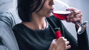 Depressed woman sitting on couch and drinking wine at home