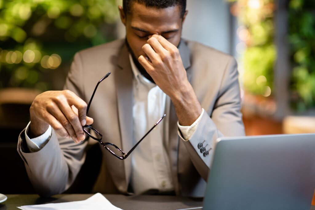 Exhausted afro manager massaging nose while using laptop