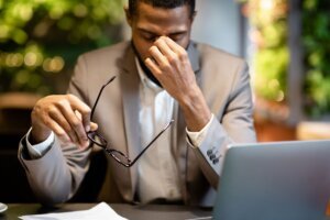 Exhausted afro manager massaging nose while using laptop