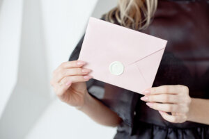 Close up photo of a female hands holding a pink invitation envelope with a wax seal, a gift certificate, a card, a wedding invitation card.