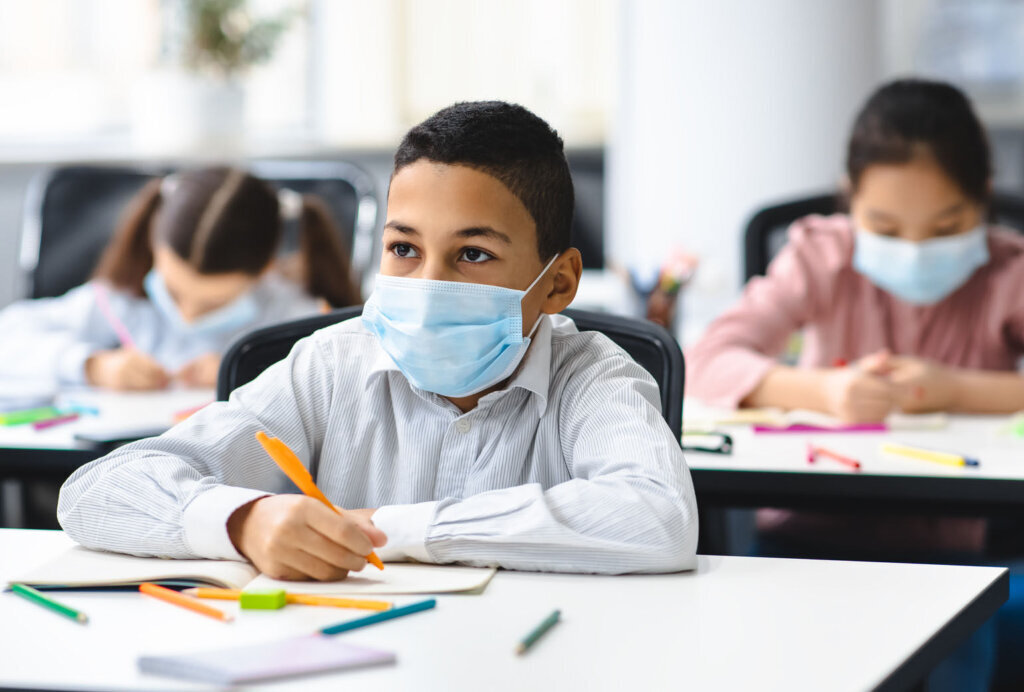 Boy in mask sitting at desk in classroom