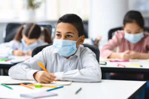 Boy in mask sitting at desk in classroom