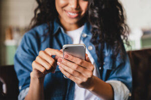 Cropped shot of an african american young woman using smart phone at home. Smiling african american woman using smartphone at home, messaging or browsing social networks while relaxing on couch