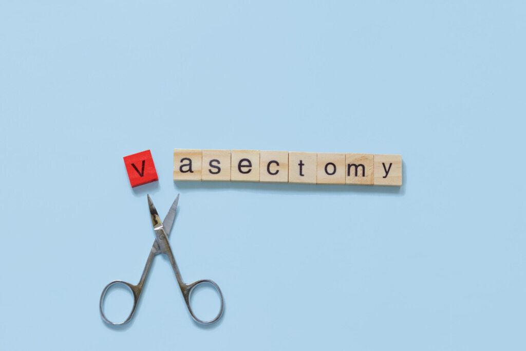 The word vasectomy made with wooden tiles on a blue background; V is red and scissors are under the word