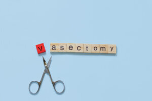 The word vasectomy made with wooden tiles on a blue background; V is red and scissors are under the word