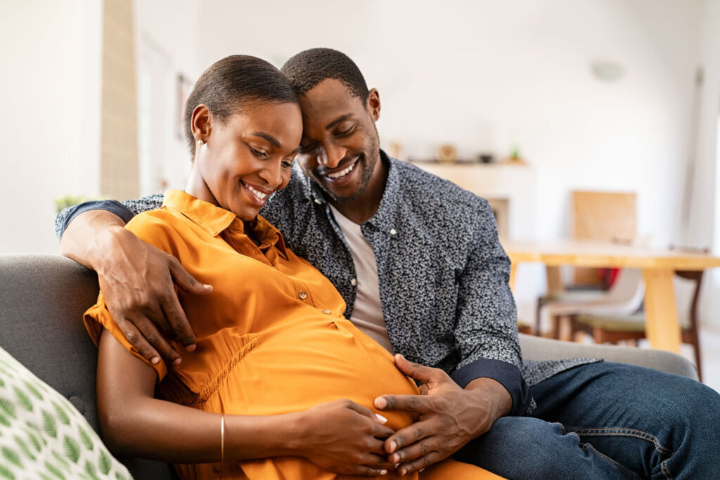 Black expectant parents sitting on sofa dreaming about their baby
