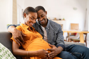 Black expectant parents sitting on sofa dreaming about their baby