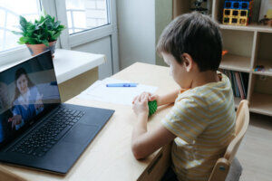 8 years old boy sit by desk with laptop and do exercise with massage ball