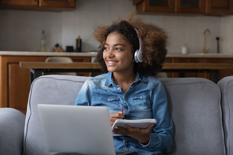 African teen student girl in wireless headphones studying at home