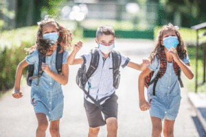 Happy schoolchildren with face masks run from the joy of returning to school during the Covid 19 quarantine.