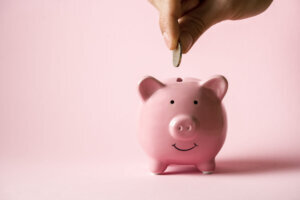 Hand puts a coin in a piggy bank.