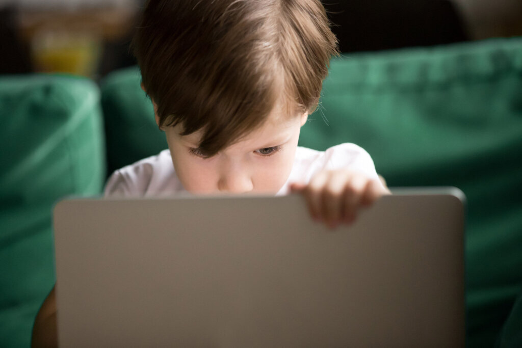 Curious kid boy secretly watching forbidden censored content on laptop