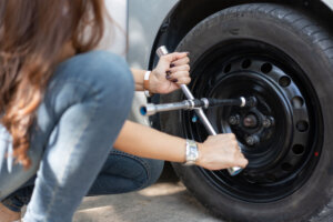 Smart and Attractive Asian woman jacks up her car and uses a wrench to change the wheel on a broken car, uses tools or equipment, tries to solve problems by self, Car Repairing and insurance concept
