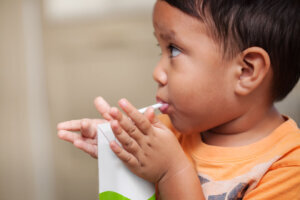 A 3 year old boy that has learned how to hold a juice box on his own and drink from a straw.