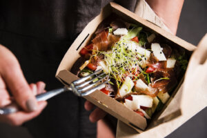 Woman's hand is holding a take away fresh salad in a lunch box.