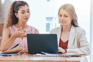 Teamwork, mentor and coaching with a leader, manager or boss talking to a business woman and working on a laptop at work. Collaboration, learning and planning with a senior supervisor and employee