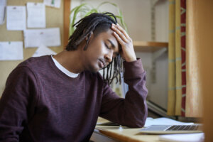 Stressed Male University Or College Student With Poor Mental Health Studying With Laptop At Desk In Room