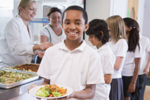 Schoolboy holding plate of lunch in school cafeteria