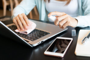 Closeup of woman hands cleaning her laptop. Disinfect surfaces, high touch and daily use item to prevent the coronavirus disease pandemic, hygiene concept.