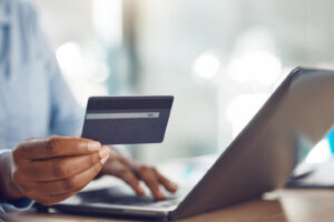 Ecommerce, online shopping and credit card payment on a laptop via the internet for easy and fast digital cash exchange. African persons hands typing banking information on fintech to transfer money