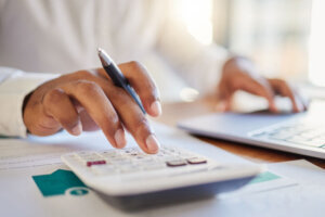 Finance, accounting and fintech, a man on a computer and calculator working out his business budget strategy. Businessman at his office desk, laptop, money management and financial investment online.