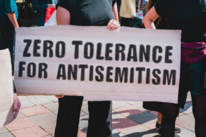 The phrase " Zero tolerance for antisemitism " drawn on a carton banner in hand. A girl holds a cardboard with an inscription. Girls on the street. Protest, march. Rally.