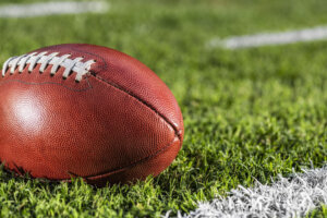 A close up of an American football sitting next to a white yard line with hash marks