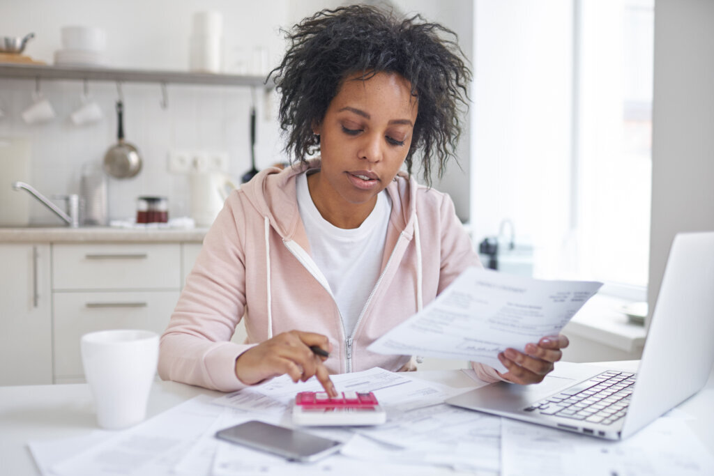 Financial literacy concept. Indoor shot of young single african american female student sitting at kitchen table, calculating expences, trying to analyze domestic dudget, thinking how to pay debt