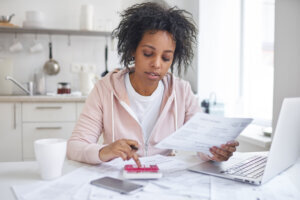 Financial literacy concept. Indoor shot of young single african american female student sitting at kitchen table, calculating expences, trying to analyze domestic dudget, thinking how to pay debt