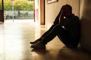 Emotional moment: man sitting holding head in hands, stressed sad young male having mental problems, feeling bad, depressed, disappointed, hopeless. Desperate man in the dark corner needing help.