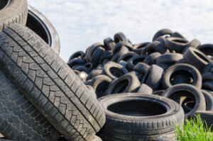 A lot of used tyres with green grass in one of against blue sky with white clouds.