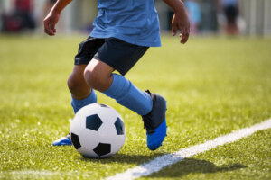 African American young boy playing soccer in a stadium pitch. Child running with soccer ball along the field white sideline. Junior soccer background