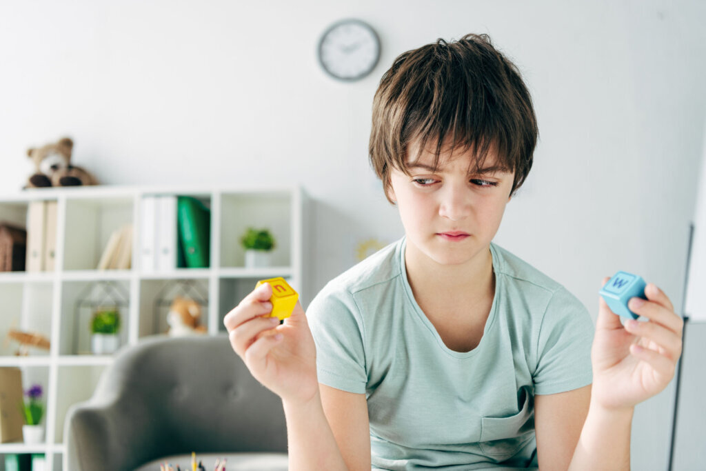 Kid with dyslexia holding wooden building blocks and looking at it