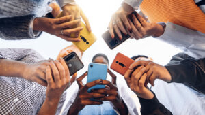 Teens in circle holding smart mobile phones Multicultural young people using cellphones outside Teenagers addicted to new technology concept