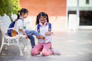 Back to school. Cute little girl kindness ties shoelaces for a friend.