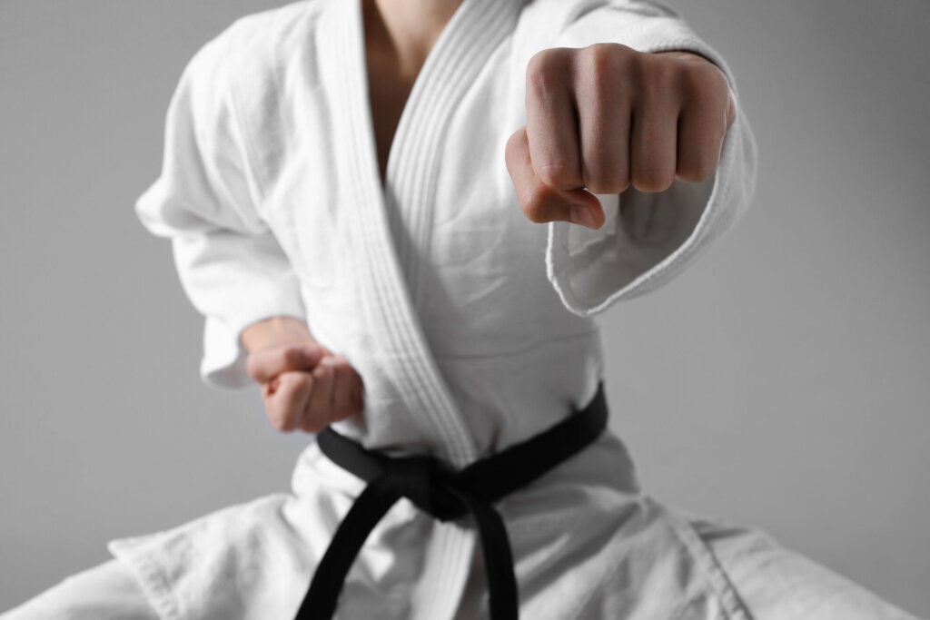 Martial arts master in keikogi with black belt against grey background, focus on fist