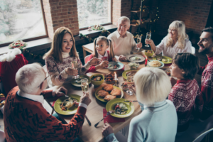 High above angle view of noel diverse family gathering. Cheerful glad grey haired grandparents, grandchildren, brother, sister, sitting at table, fun joy house party, feast, tasty yummy food, clink