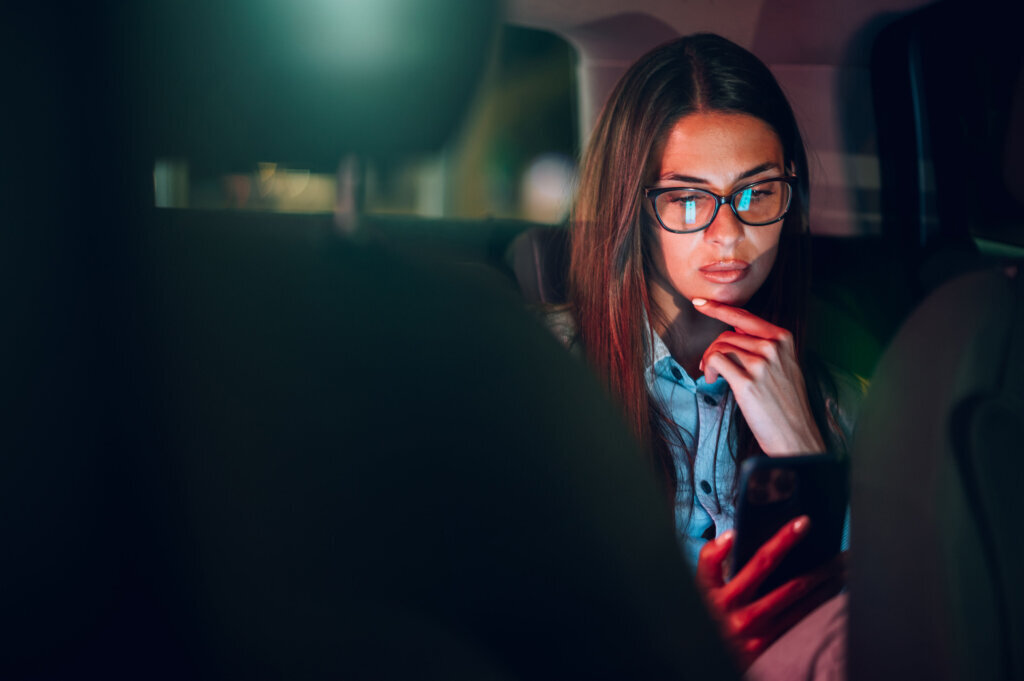 Business woman using smartphone while sitting in a backseat of a car at night