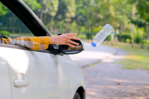 Woman hand throw clear bottle with blue cap out from car window with the concept human garbage destroy environment